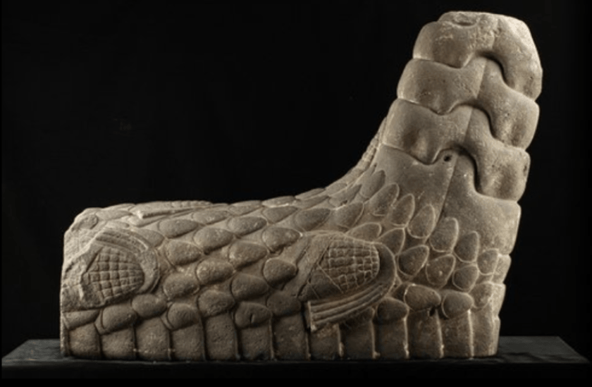 escultura que representa una cola de serpiente de cascabel con seis mazorcas de maíz grabadas y crótalo